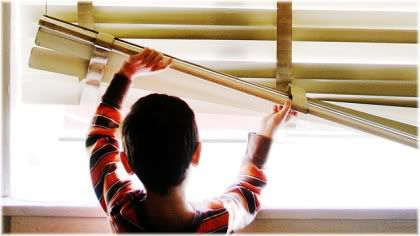 boy lifting up blinds looking out window